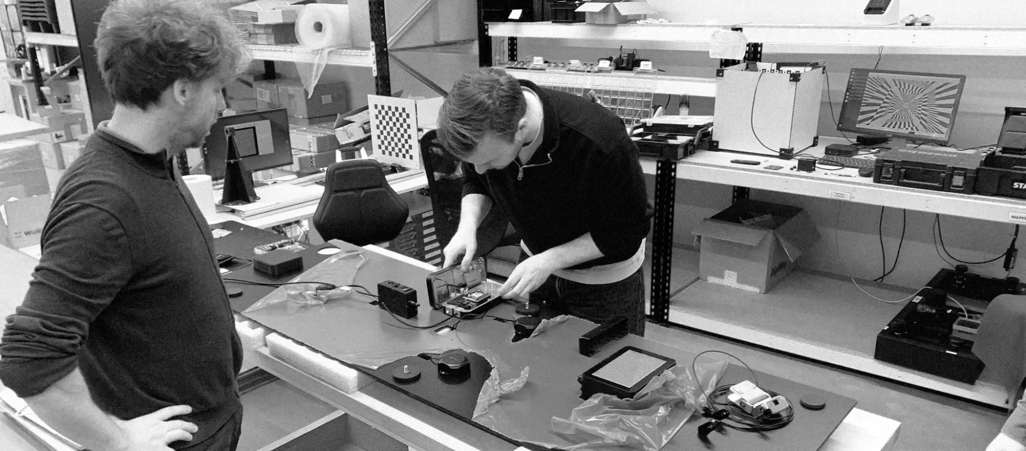 Two people working together at a workbench, assembling an electronics housing in a workshop